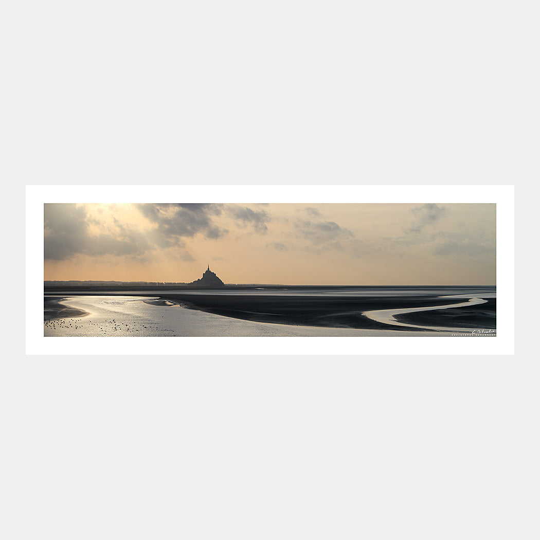 Photographie panoramique de la baie du Mont-Saint-Michel à marée basse avec un trait de lumière perçant les nuages sur l'abbaye du Mont-Saint-Michel au couchant, Cotentin, Manche, Normandie, France.